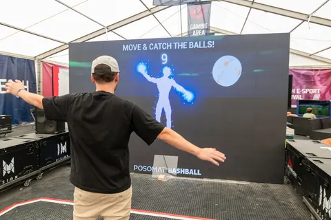 A player stands with outstretched arms in front of the Bashball LED wall, his body appears as a figure in the game