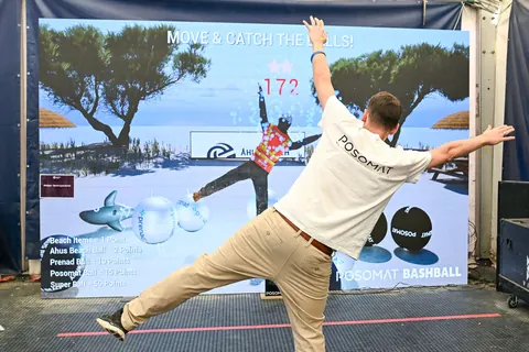 A man plays Bashball with outstretched arms in front of an LED wall on the beach