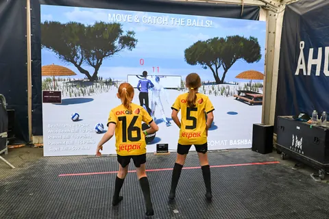 Two children in sportswear play Bashball in front of an LED wall with a beach motif