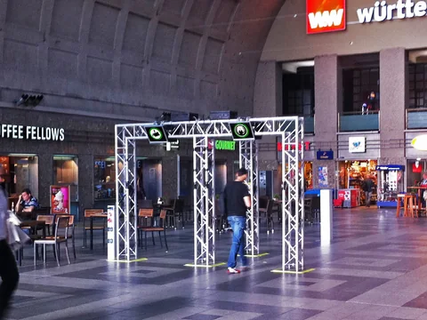 Truss archways with displays in a station concourse, passers by walk through them