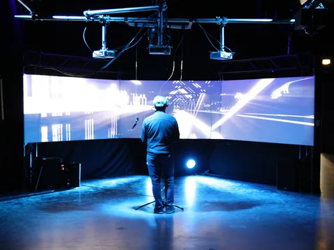 A visitor stands in front of a large curved projection surface with an abstract 3D world